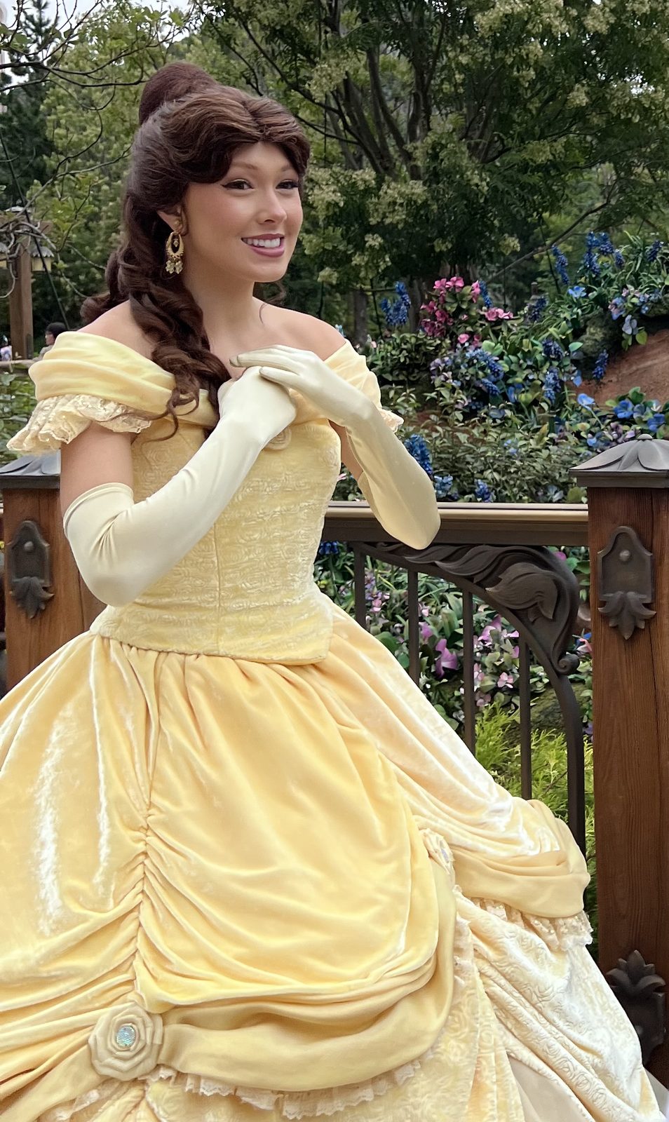 黄色いドレスのベルが、お花と柵のそばで笑っているところ