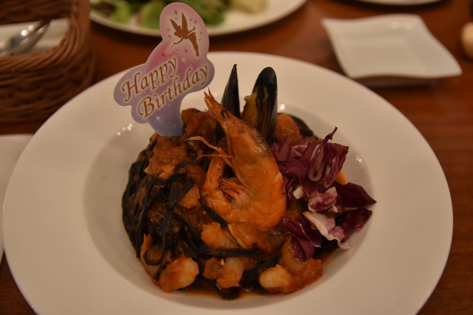 黒いパスタに、えびとムール貝とトマトソース。「Happy Birthday」のティンカーベルの飾りつき