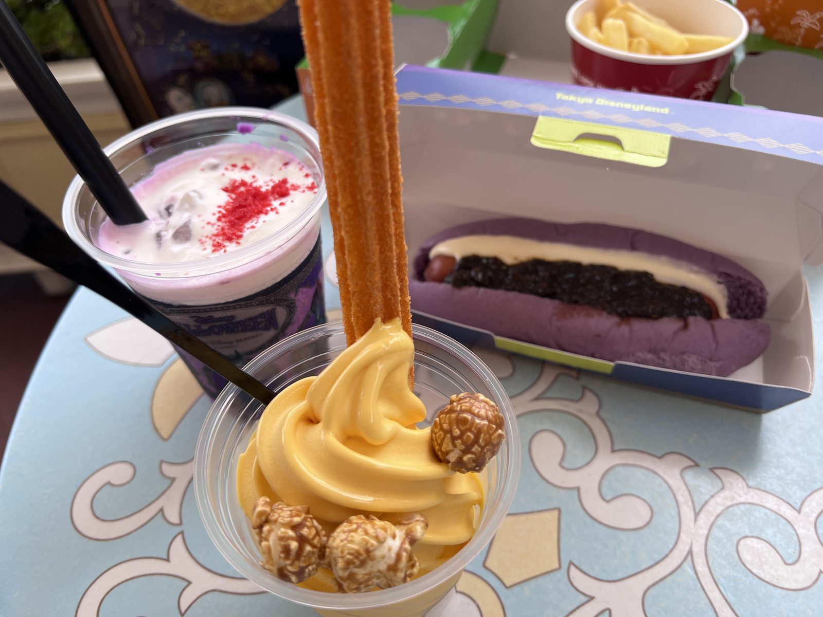 紫のドリンク、紫のパンのホットドッグ、ポテト、かぼちゃのソフトクリームにチュロス